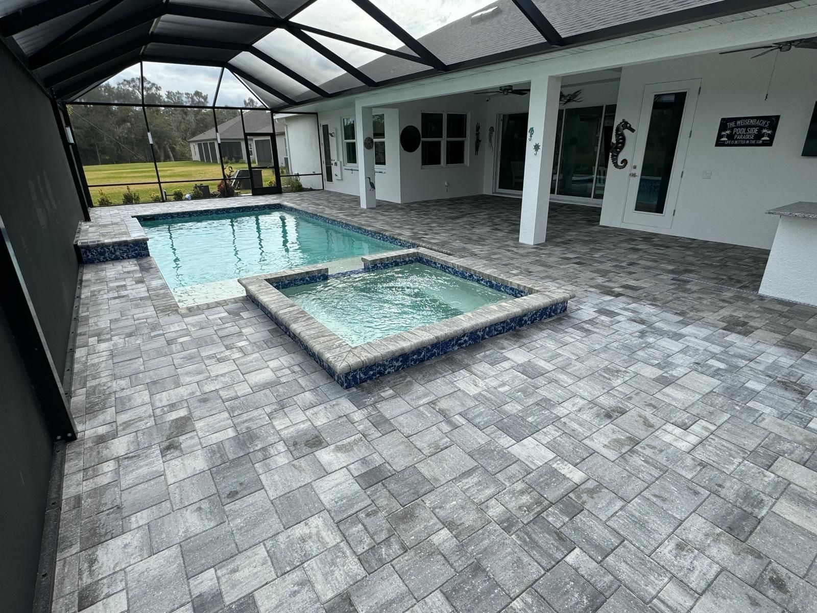 Covered patio with rectangular pool and raised spa, featuring gray pavers and white exterior walls.