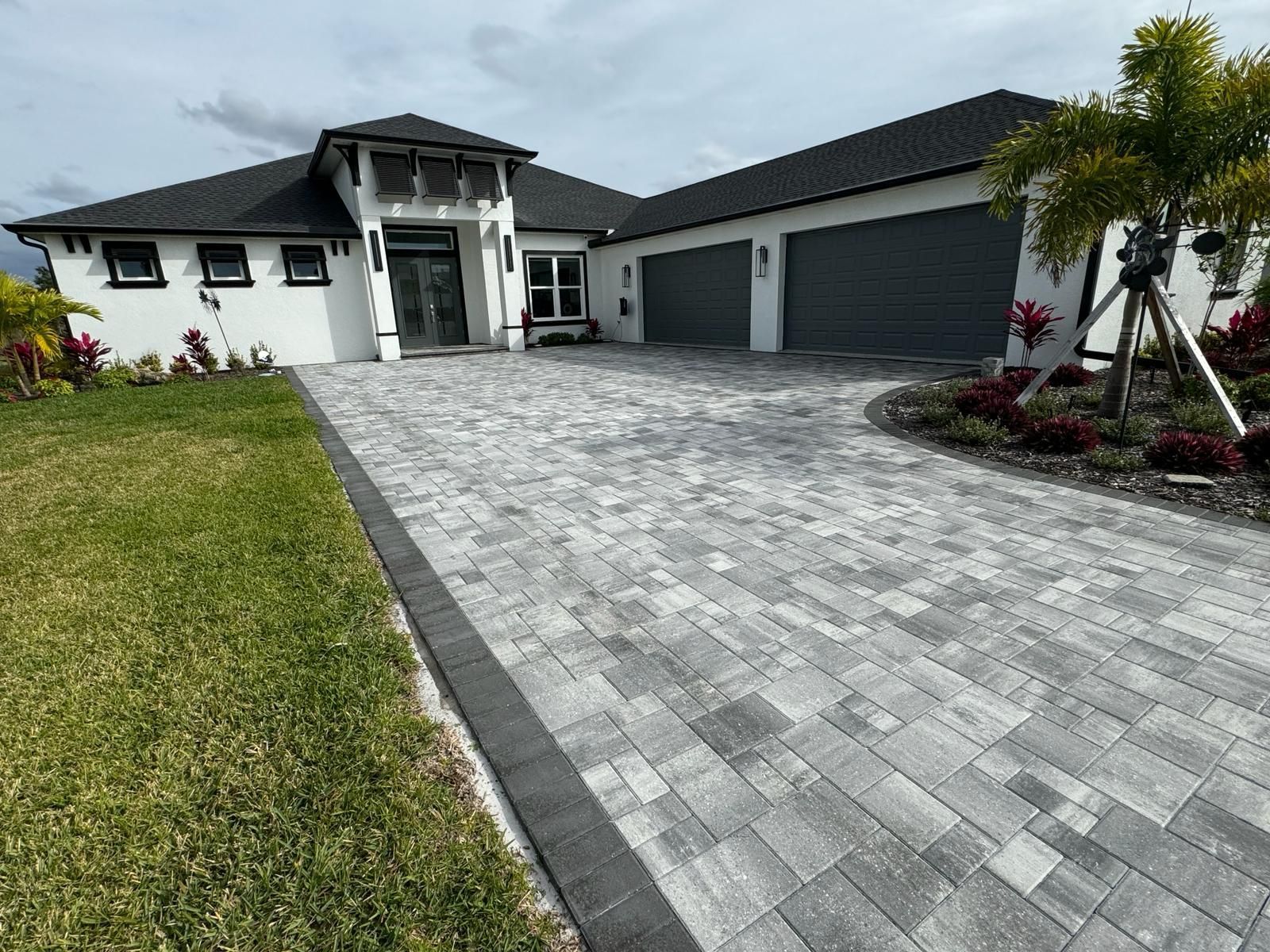 Modern white house with dark roof, gray driveway, two-car garage, and landscaped front yard