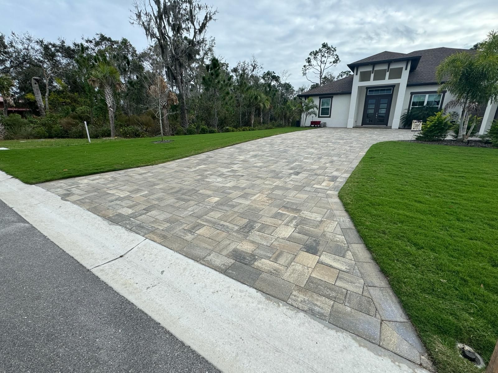 Wide stone driveway leading to a modern house with a green lawn on both sides