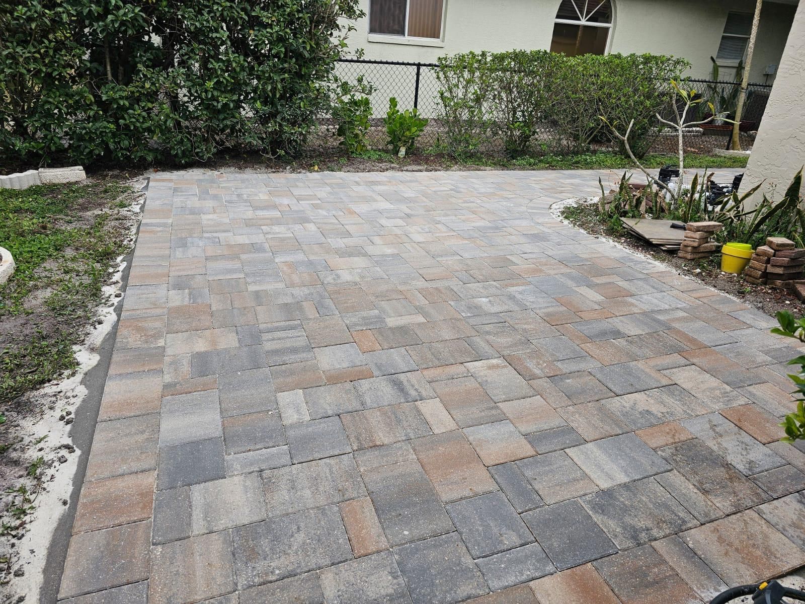 Stone-paved driveway beside a house, bordered by shrubs and garden plants.