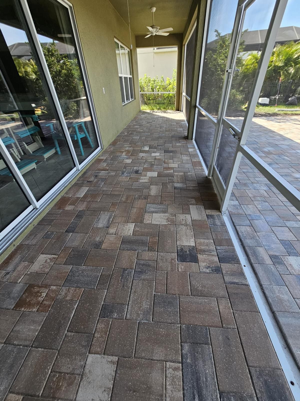Covered brick walkway beside sliding glass doors and a stucco wall, leading to a yard with trees.