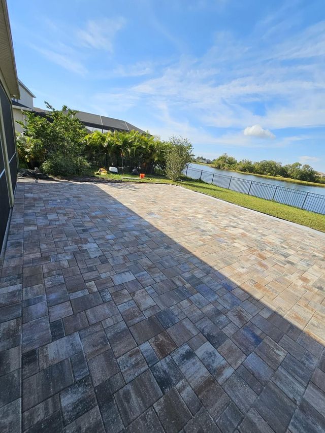 Stone patio beside a lawn and waterfront, with trees and a blue sky in the background.