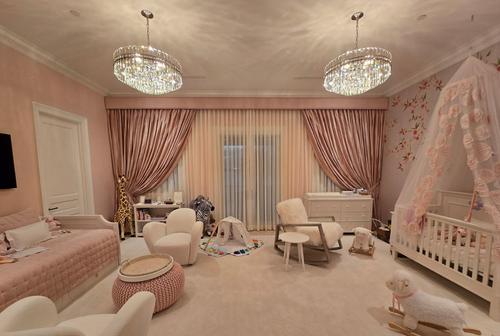 Pink nursery with crib, daybed, chandelier, and rocking chair.
