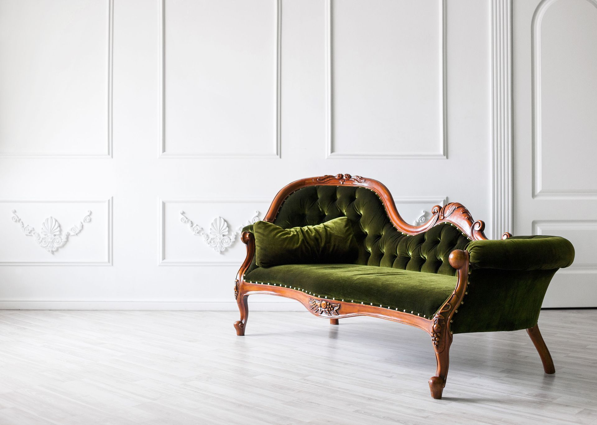 Green velvet chaise lounge against white paneled wall and floor.