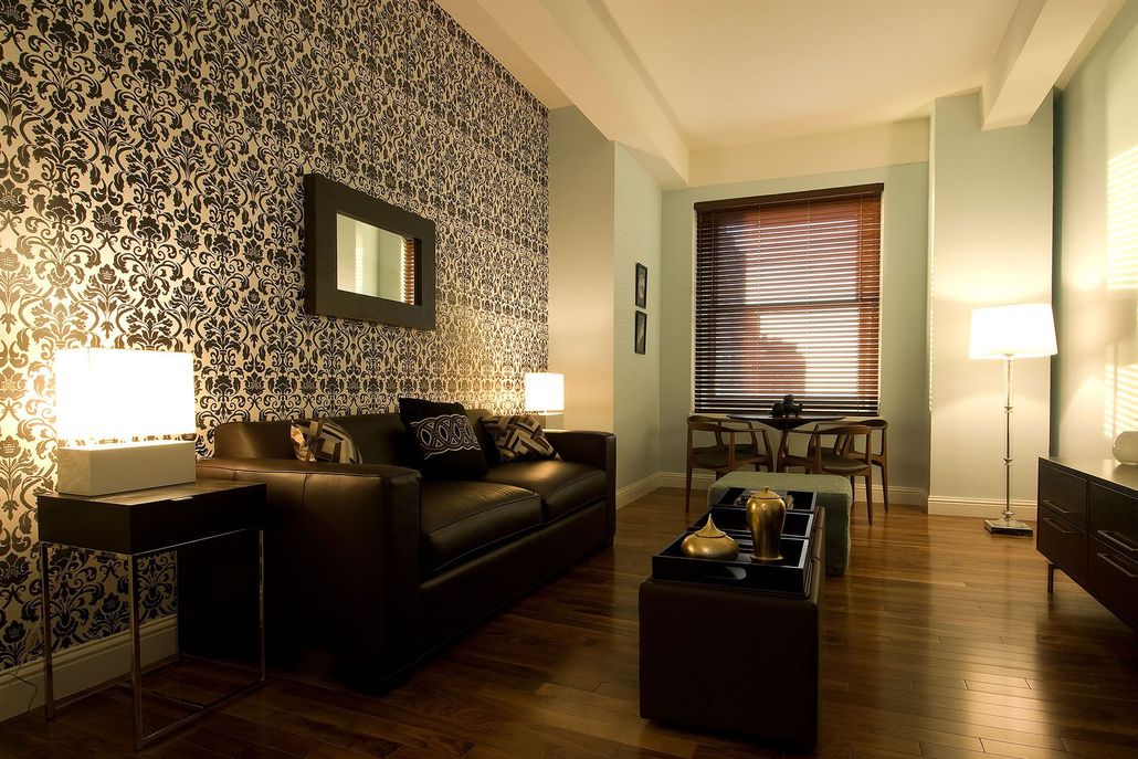 Modern living room with black sofa, patterned wallpaper, lamps, and hardwood floor
