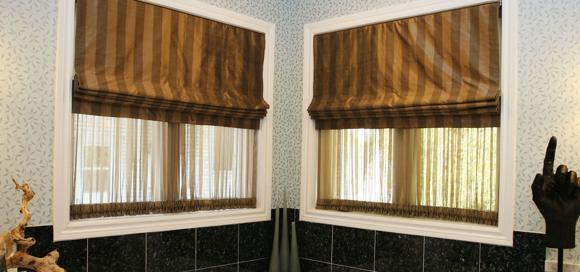 Two windows with brown striped valances and sheer curtains in a light patterned room