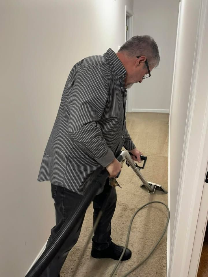 Man cleaning carpet in a hallway with a carpet cleaner. Beige carpet, white walls.