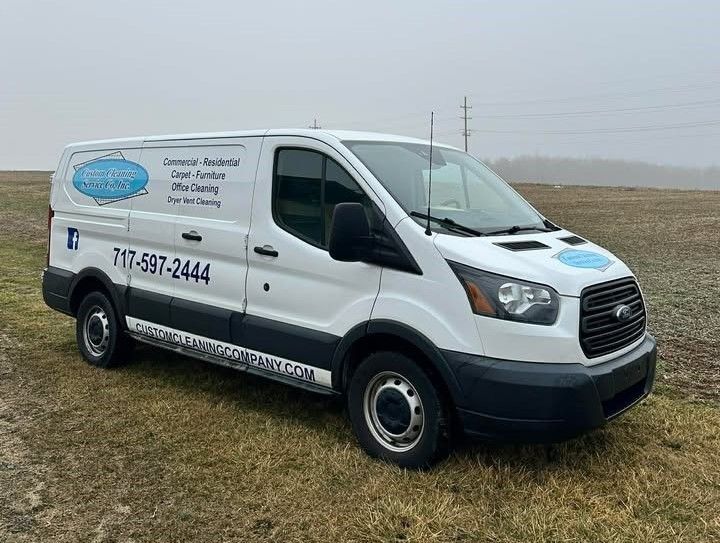 White Ford Transit van with business logo and phone number on the side, parked in a grassy field.
