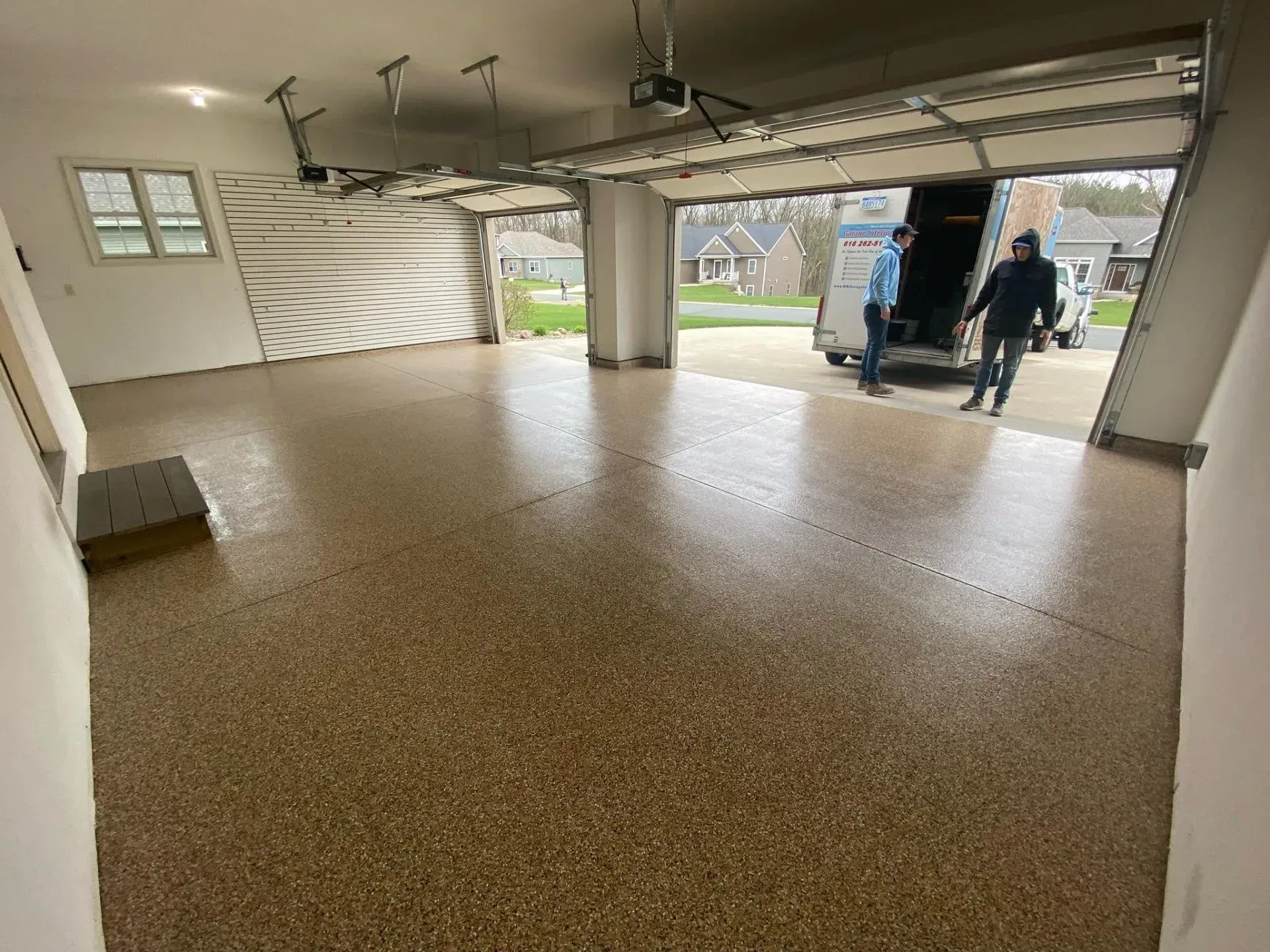 Spacious empty garage with speckled floor, open door, and two people standing outside.