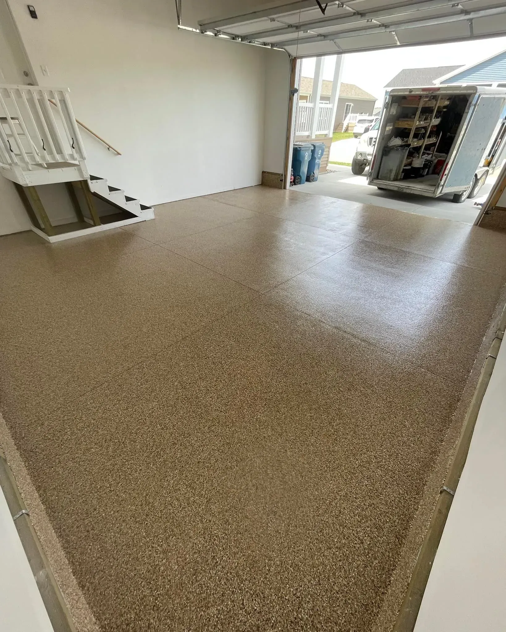 Empty garage with a speckled tan epoxy floor and open doorway to a work area outside