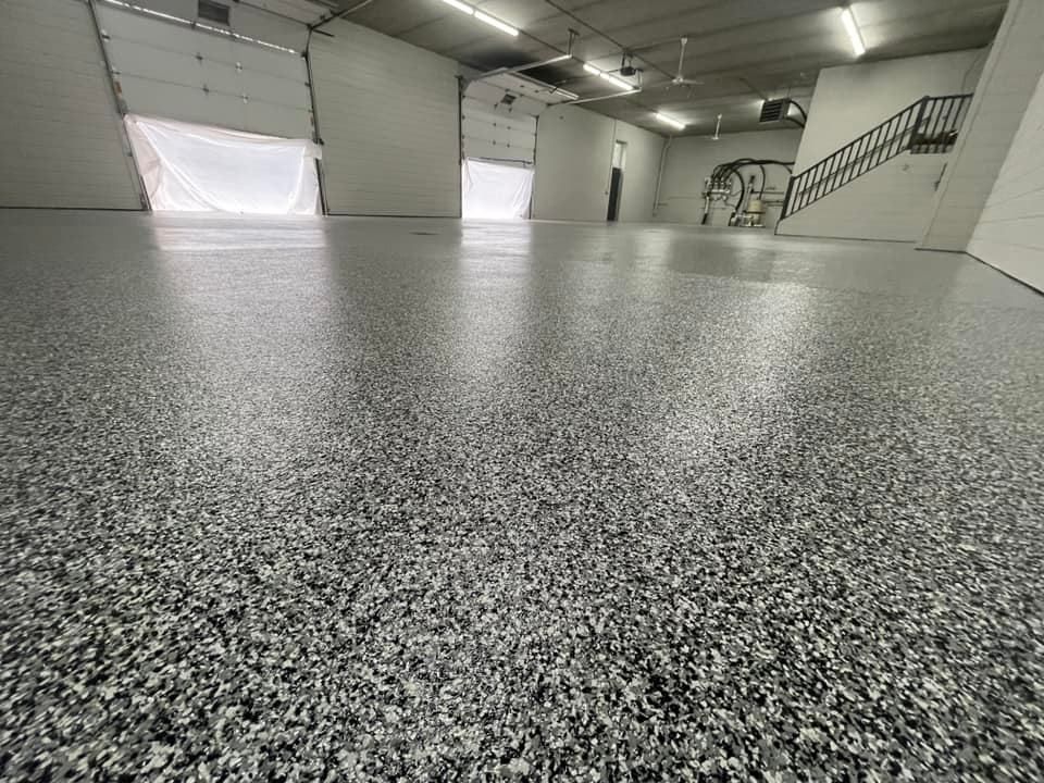 Spacious empty garage with a speckled gray floor, white walls, and a staircase in the back right.