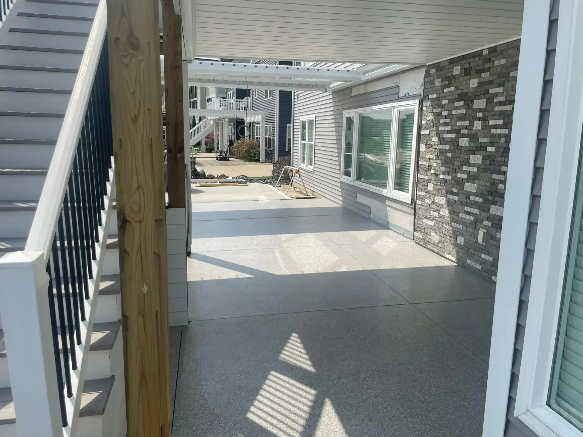 Covered apartment patio with stone wall, windows, and railing casting shadows on the concrete floor.