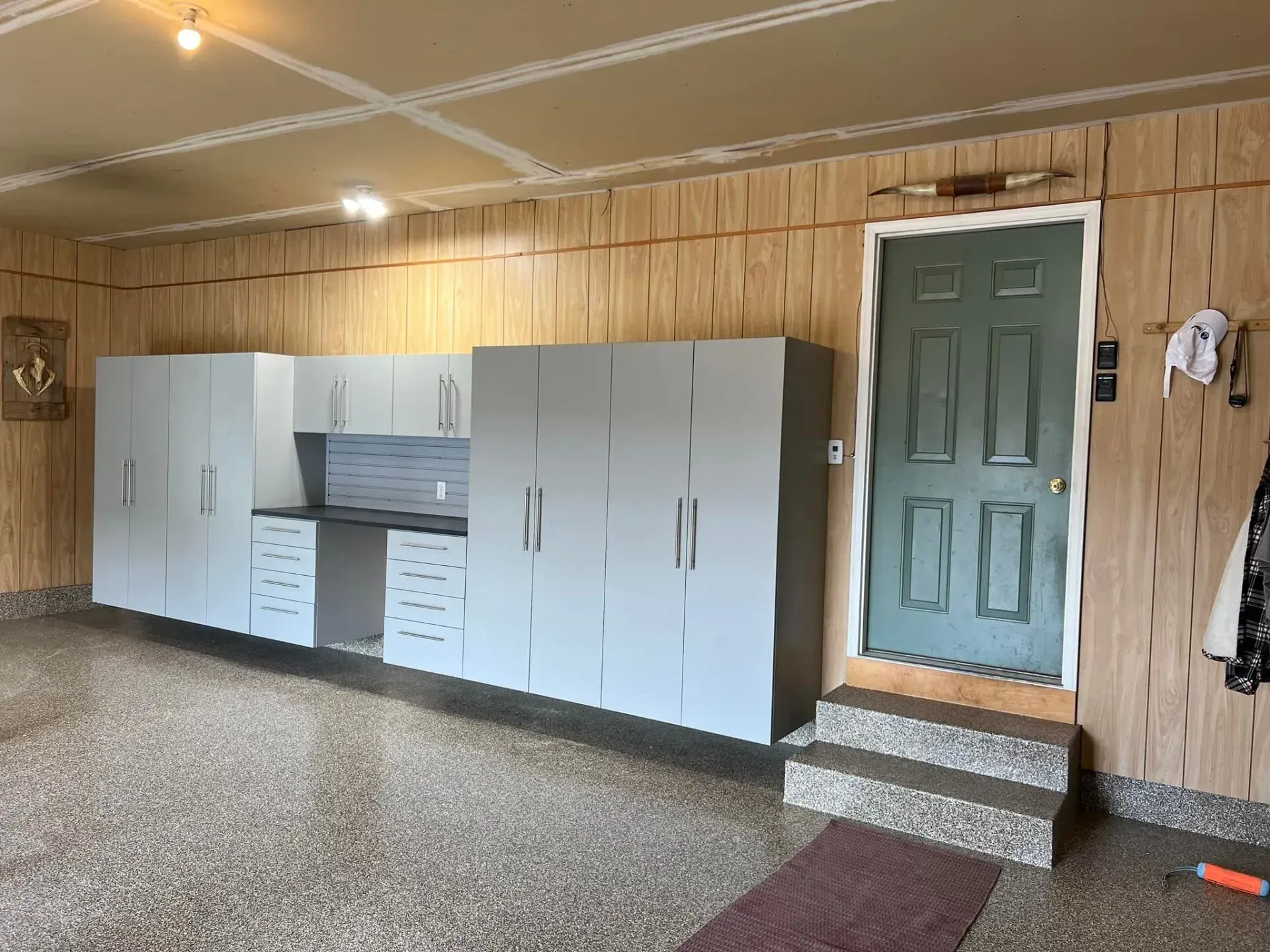 Wood-paneled room with white storage cabinets, a green door, and carpeted floor.