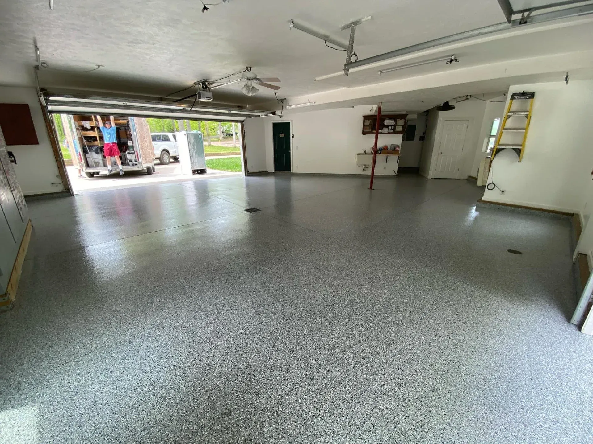 Empty garage with speckled epoxy floor, open door, shelves, and ladder on the wall.