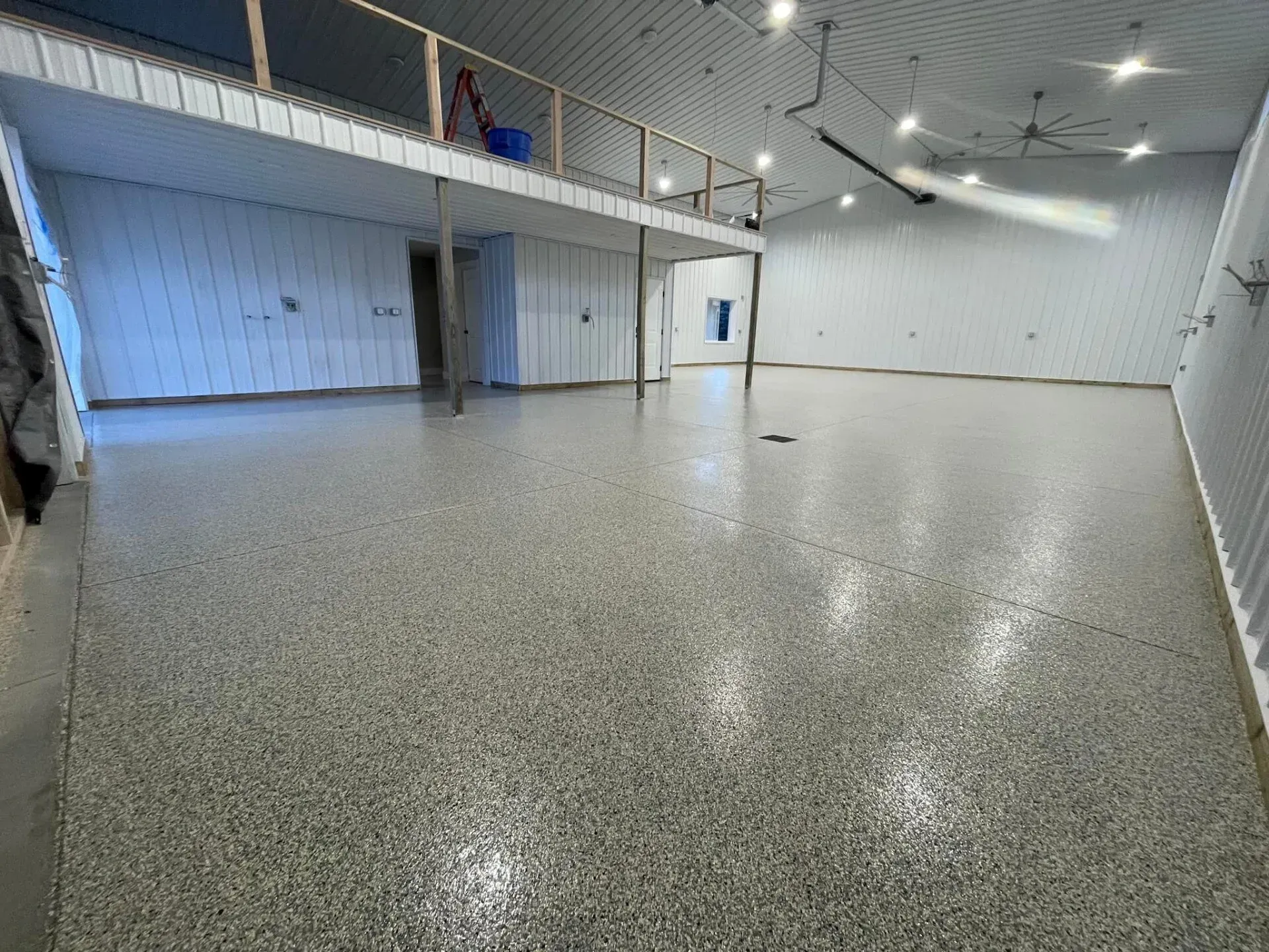 Empty indoor hall with glossy speckled floor, white walls, and a mezzanine balcony railing.