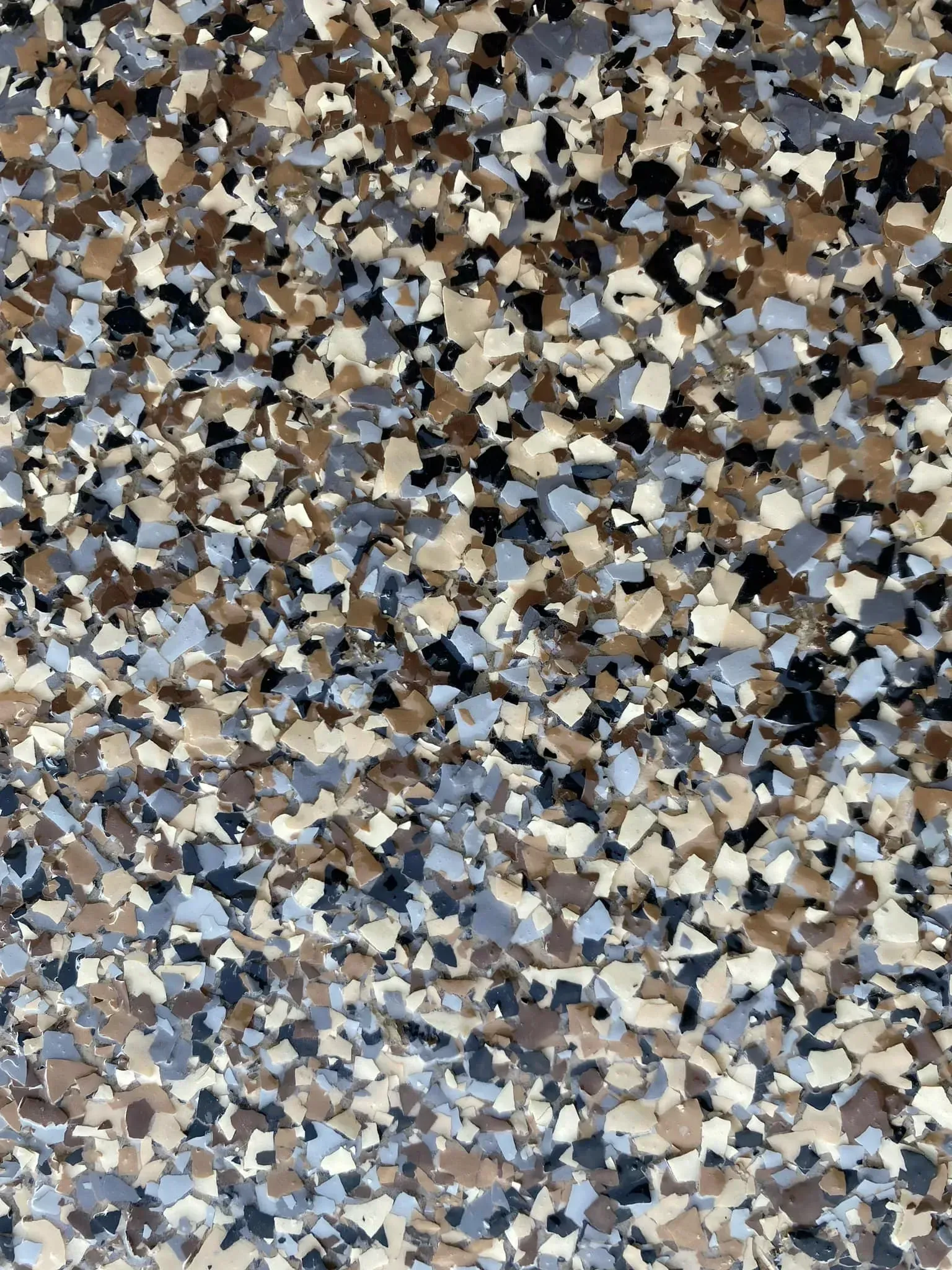 Abstract mosaic of small tan, gray, black, and blue pebbles filling the frame