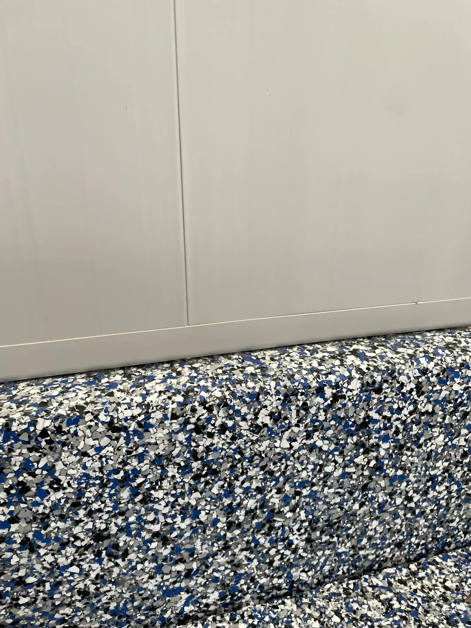 Blue speckled carpet beneath a plain light gray wall with a vertical seam.