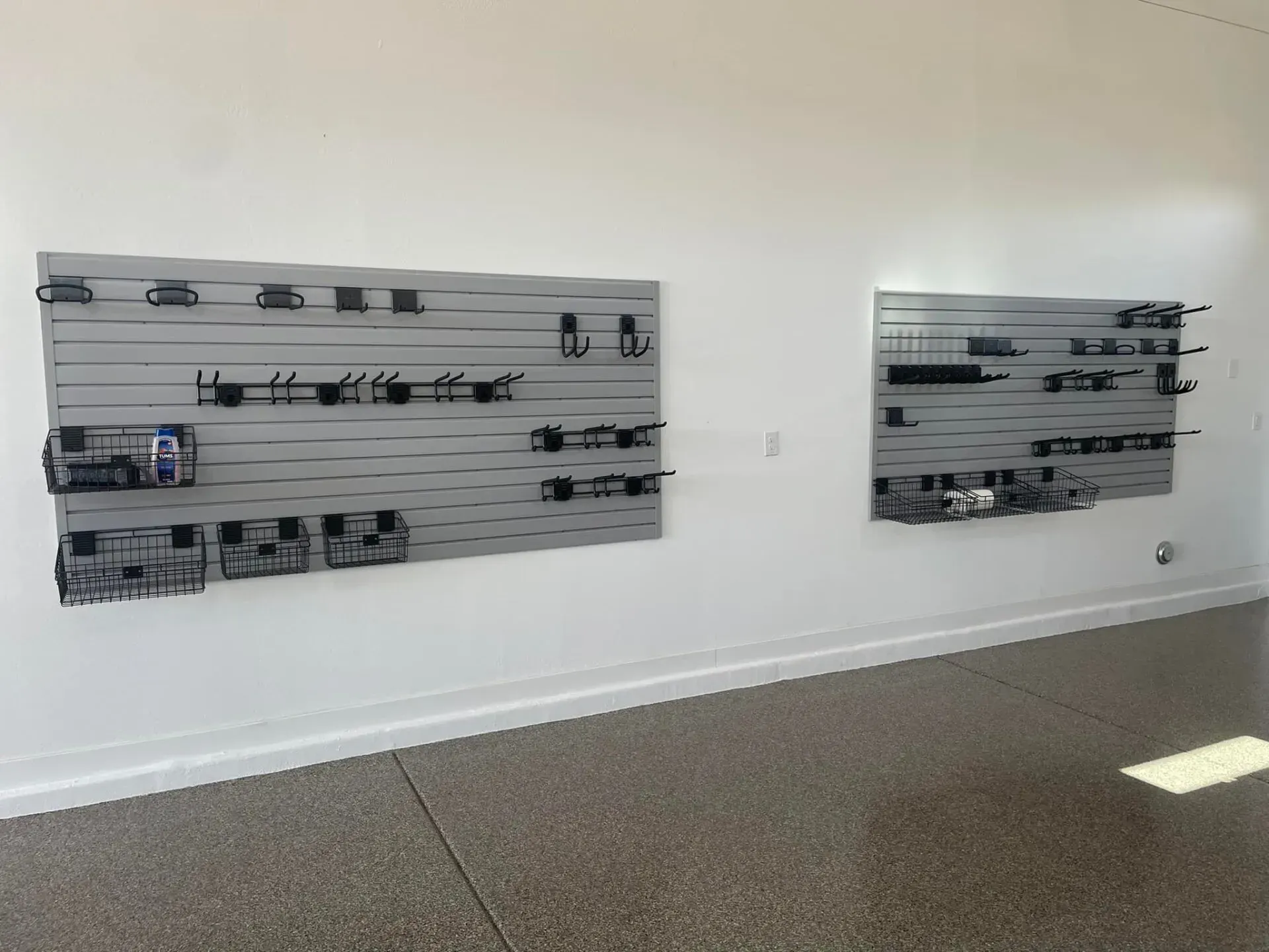 White gallery wall with two abstract metal wall sculptures above a speckled floor