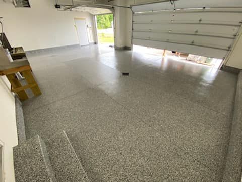 Empty garage with speckled epoxy floor, open door, and bright daylight outside