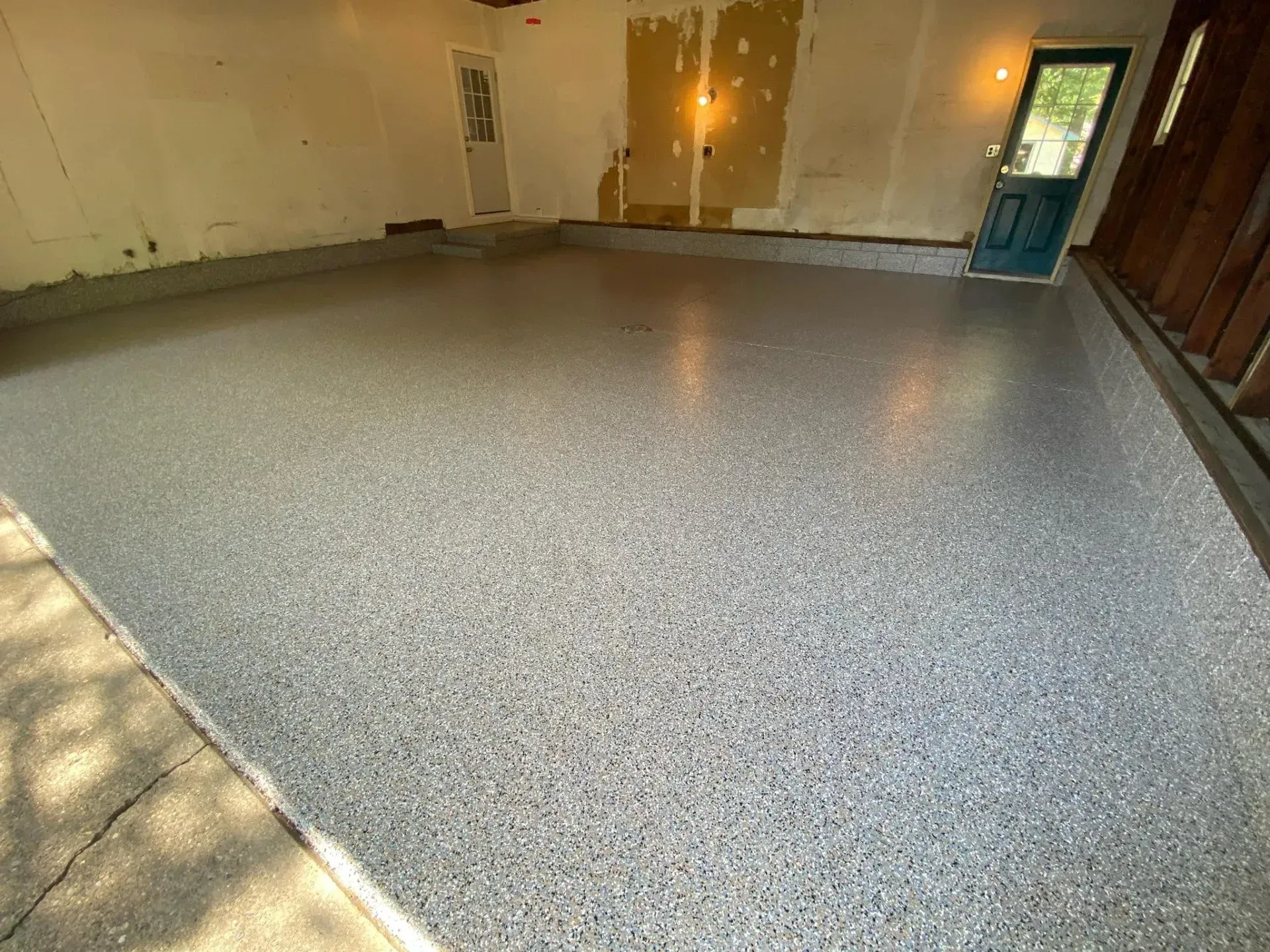 Empty room with speckled gray floor, white walls, and a glass door on the right.