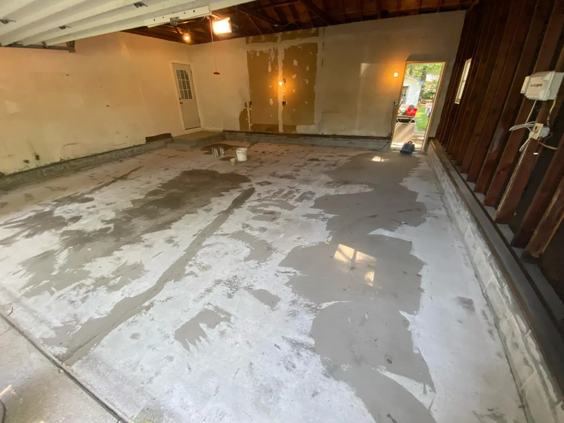 Empty unfinished garage with concrete floor, exposed framing, and daylight from an open door.
