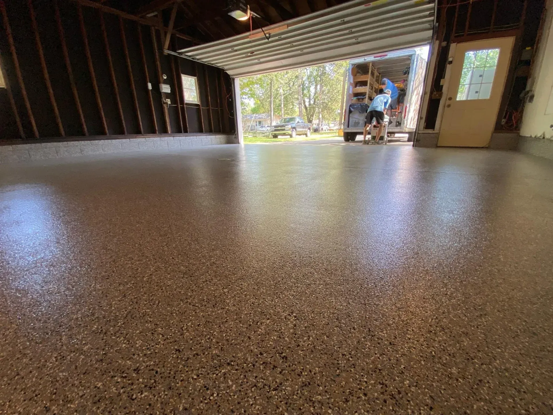 Empty garage with a speckled floor and an open door showing a person outside.