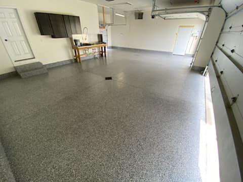 Empty garage with gray epoxy floor, wall-mounted TV, workbench, and overhead garage door.