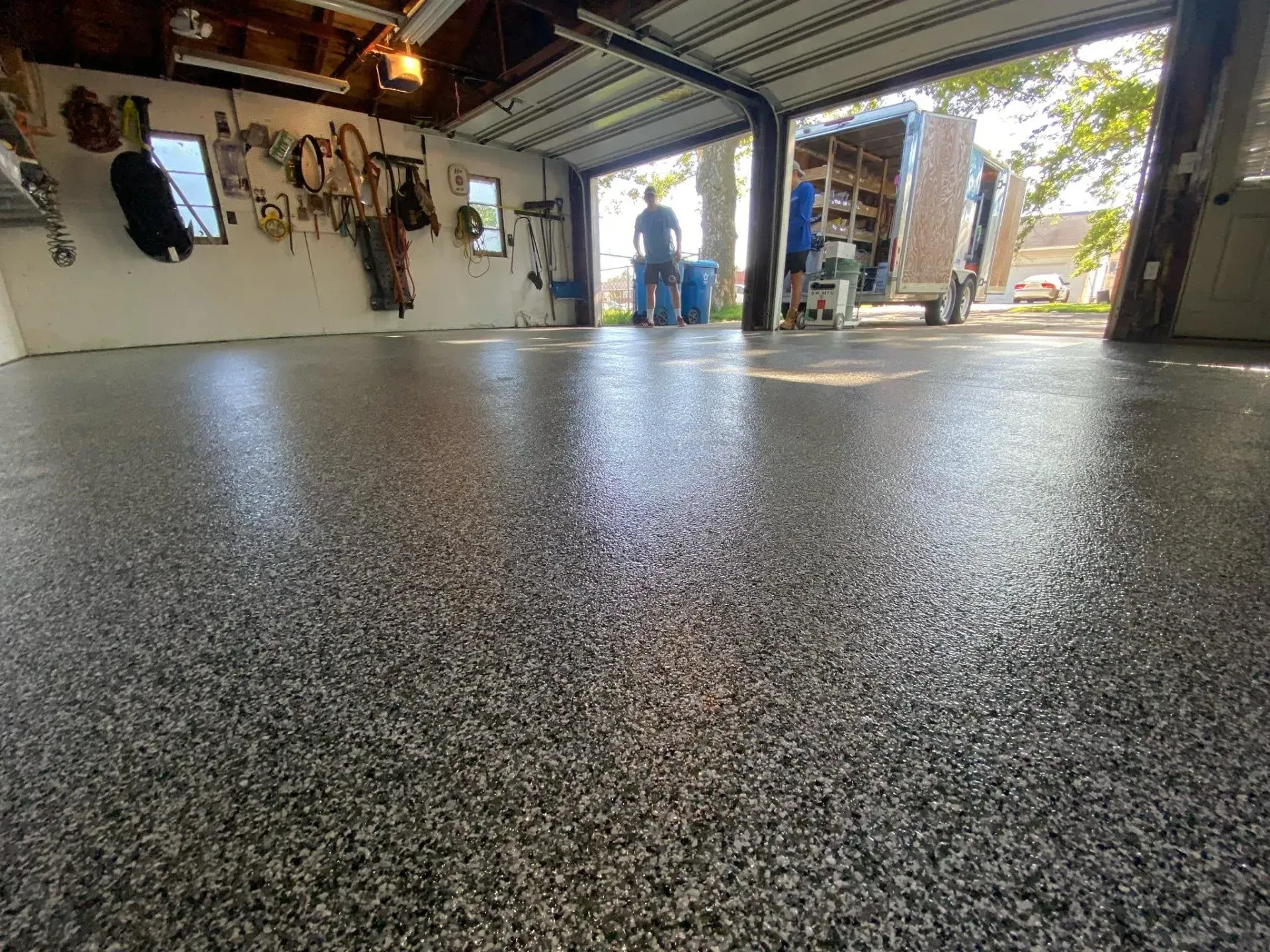 Open garage with speckled epoxy floor and a person standing in the background near the doorway.