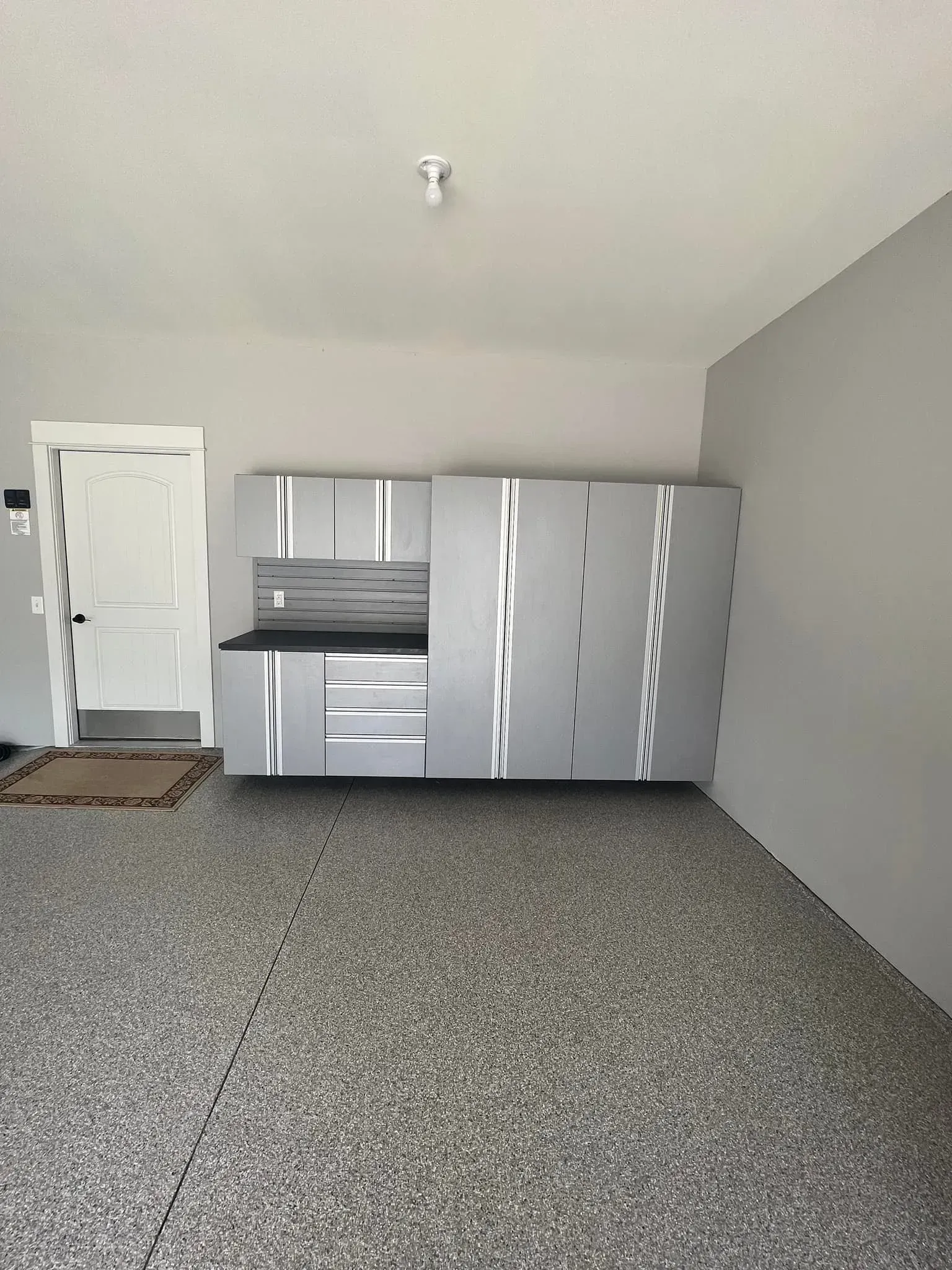 Empty room with gray walls and carpet, white door, and silver storage cabinets along the back wall