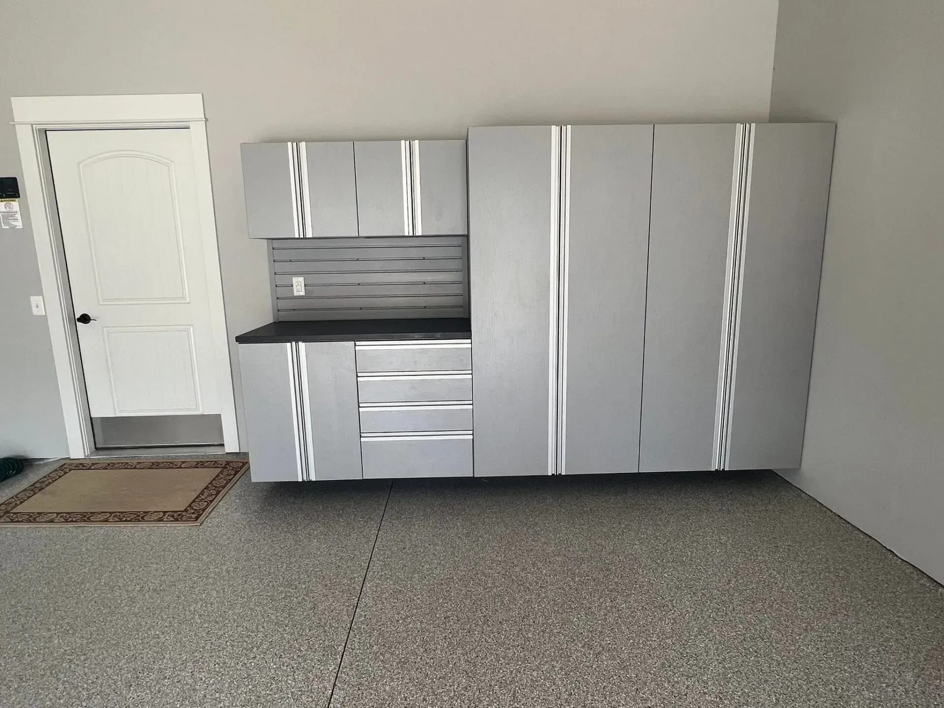 Empty garage with gray cabinets, white door, and speckled floor.