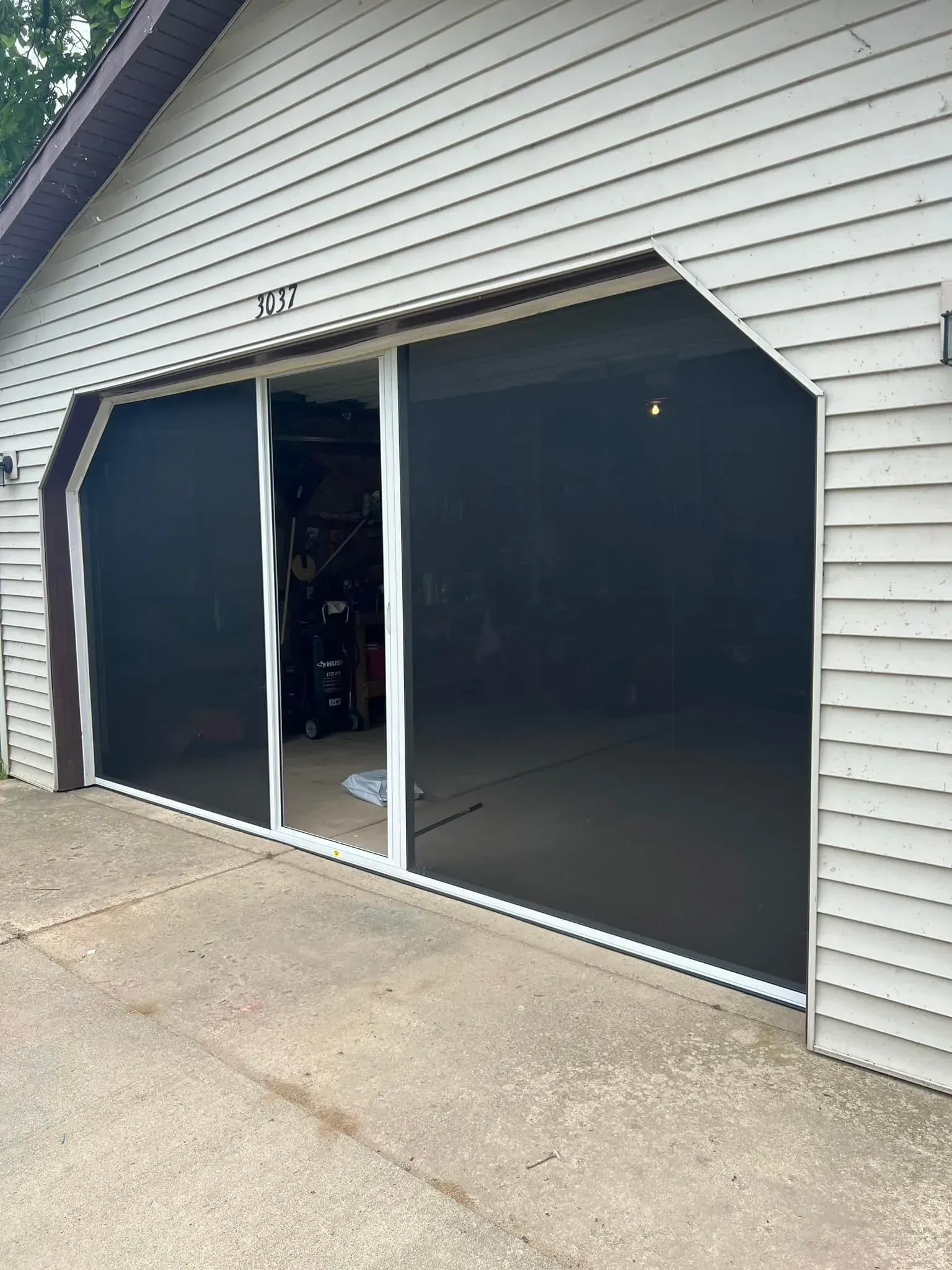 Open double garage door with dark screens on a light gray house exterior