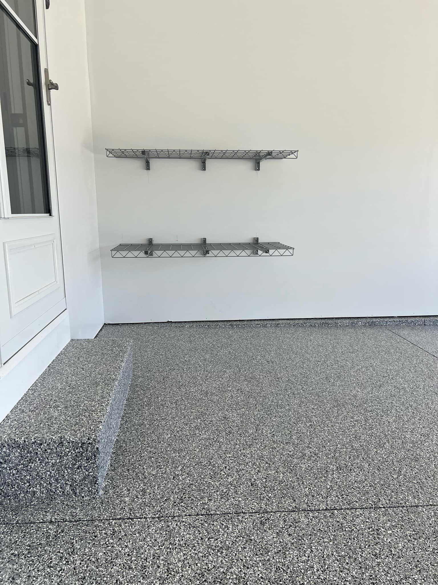 White wall with two metal bike racks beside a glass door over a pebble-textured floor.