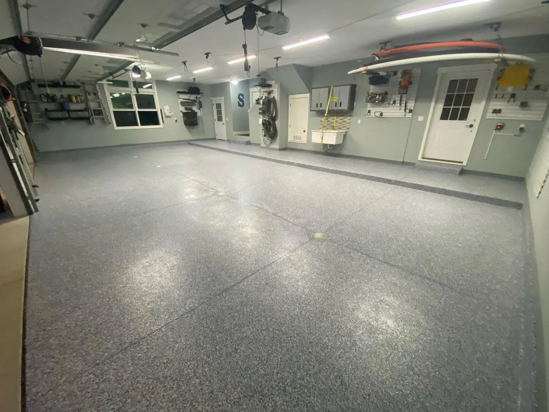 Empty garage with gray epoxy floor, white walls, overhead lights, doors, and cabinets.