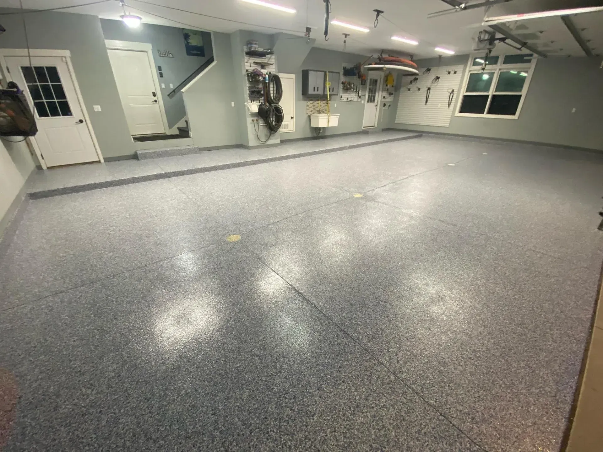 Empty speckled epoxy-floor room with gray walls, doors, windows, and utility panels