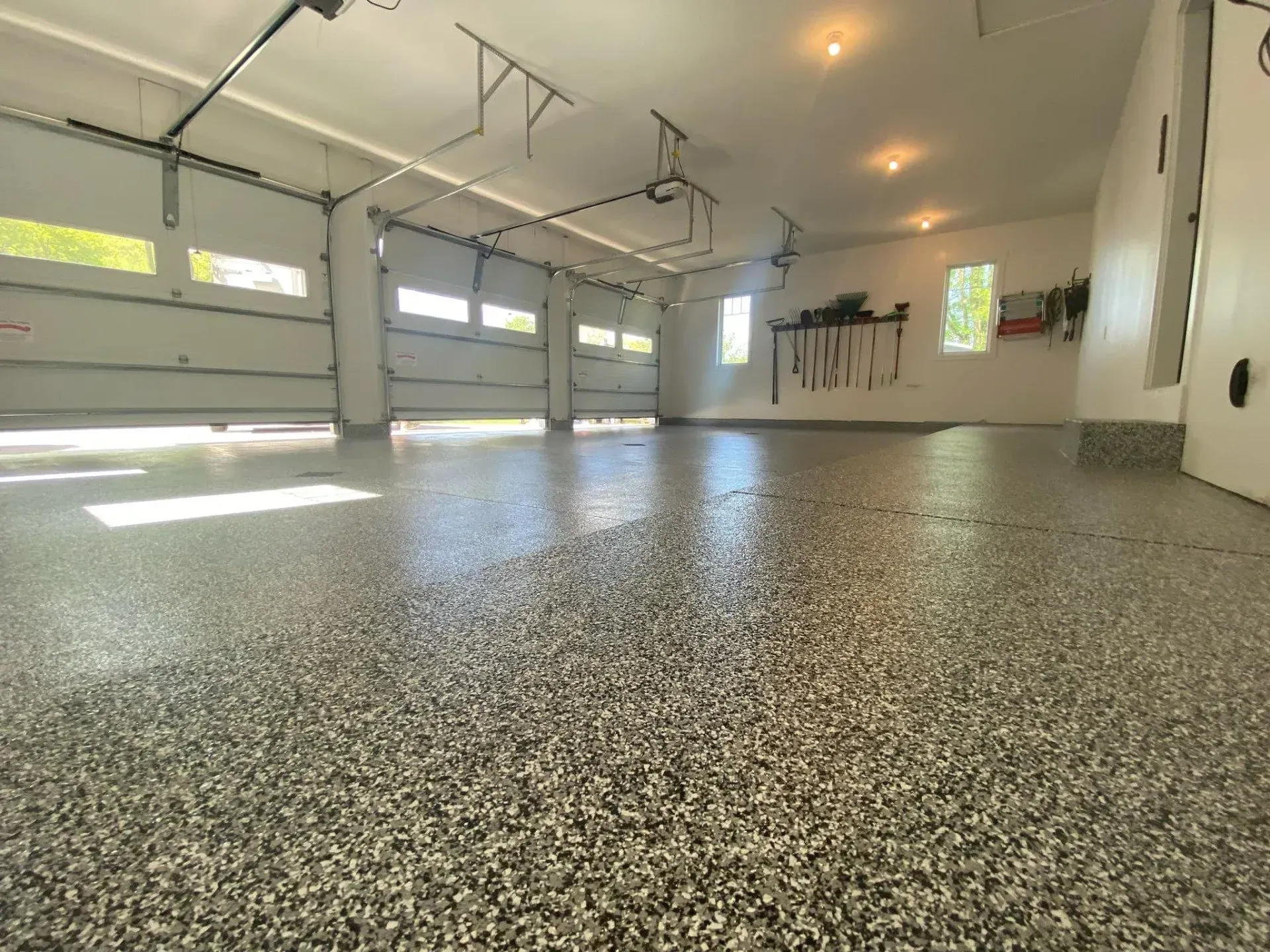 Spacious empty garage with speckled epoxy floor, white walls, and sunlight streaming through windows.