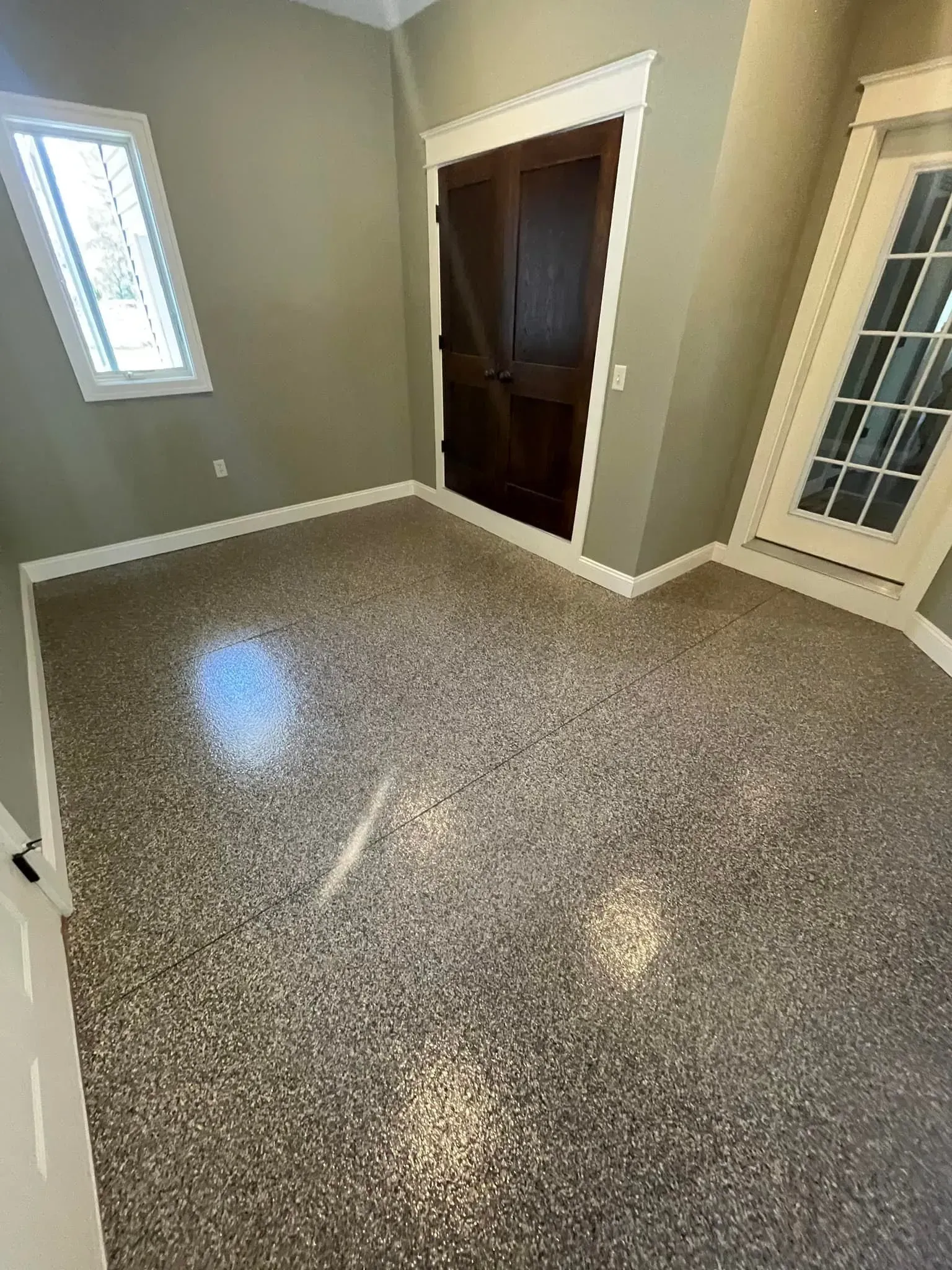 Empty room with speckled flooring, beige walls, a window, and two doorways.