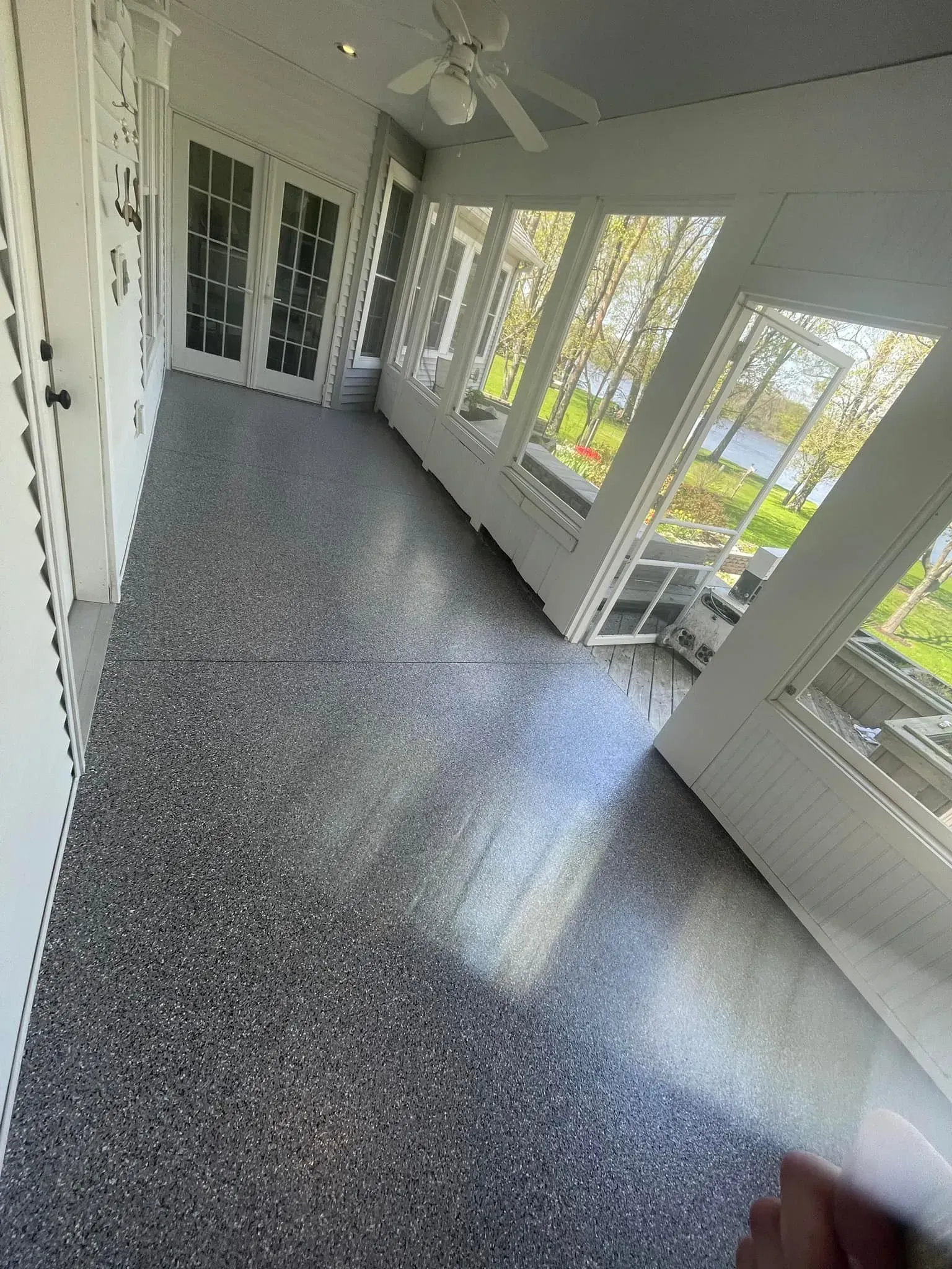Sunroom hallway with speckled gray floor, white walls, and large windows overlooking greenery