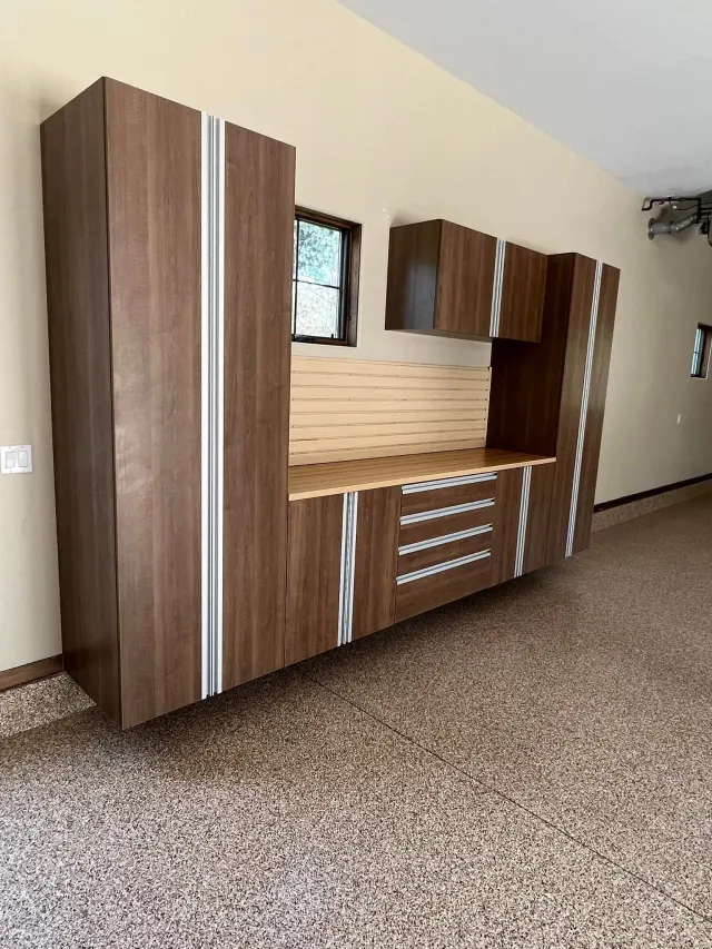 Wooden wall unit with cabinets, shelves, and drawers in a beige room with speckled carpet.