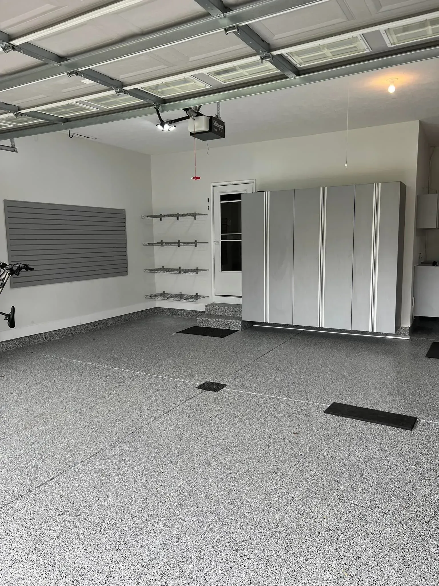 Empty garage with gray speckled floor, metal cabinets, and wall-mounted storage shelves under open ceiling.