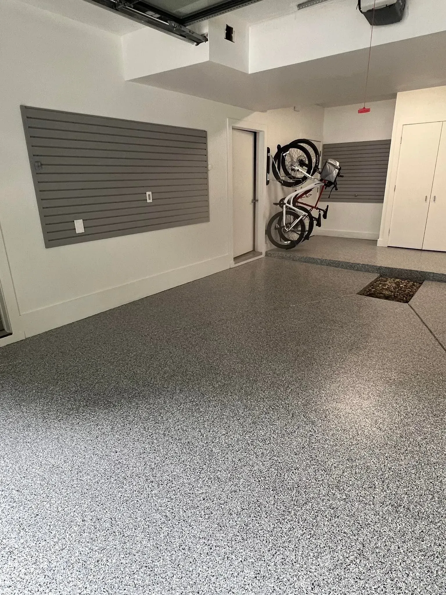 Empty garage with gray speckled floor, wall-mounted storage panels, and a bicycle hanging near the back wall.