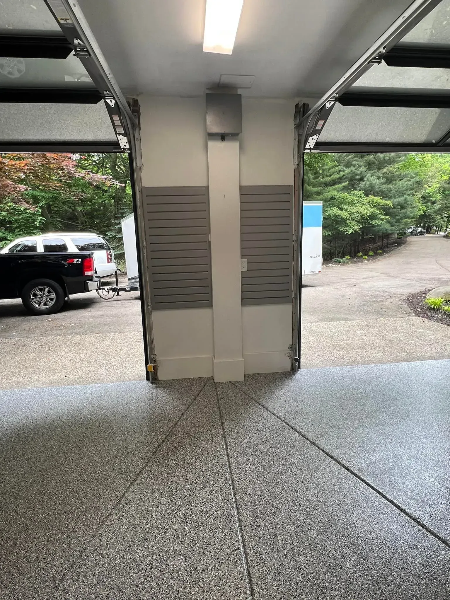 Covered garage with white support column, parked black truck, gravel driveway, and green trees outside.