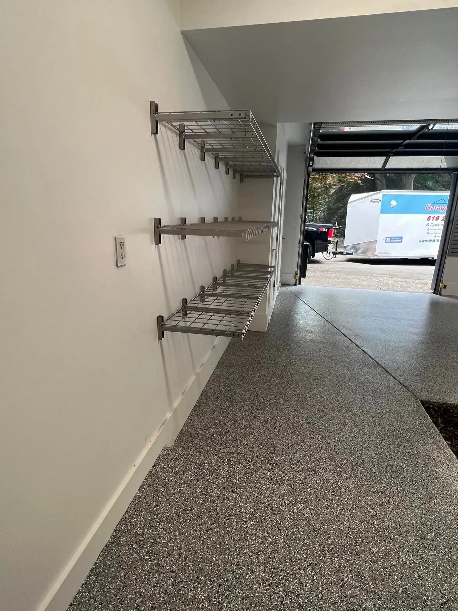 Wall-mounted metal racks in a garage opening to a driveway and parked van outside