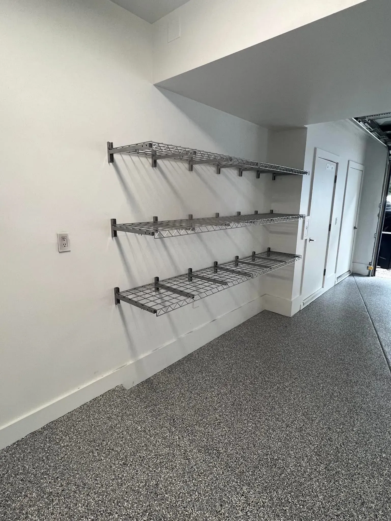 Hallway with wall-mounted metal shelves and speckled carpet flooring