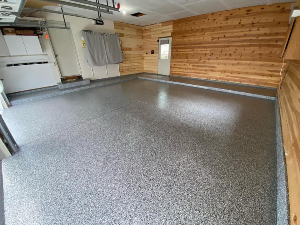 Empty garage with speckled gray epoxy floor, wood-paneled wall, and white garage door opener.