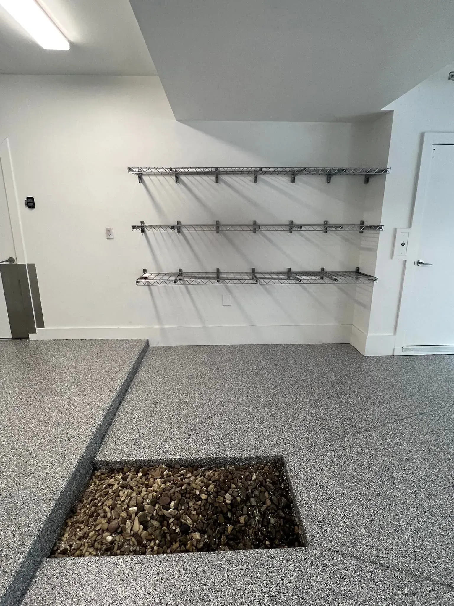 Indoor stair landing with metal handrails, a white door, and a recessed rectangular planter in speckled flooring.