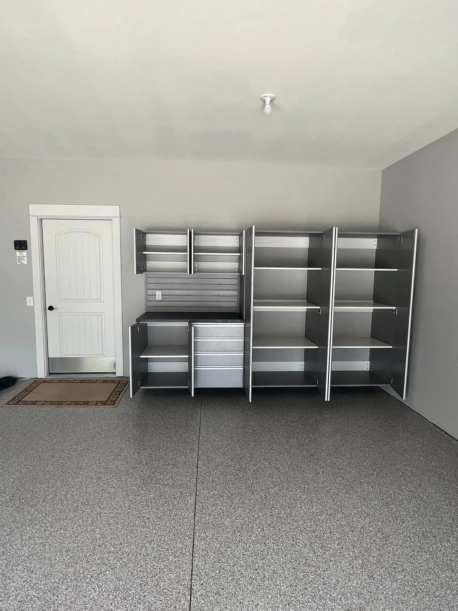 Empty garage with gray carpet, white door, and metal shelving along the back wall.