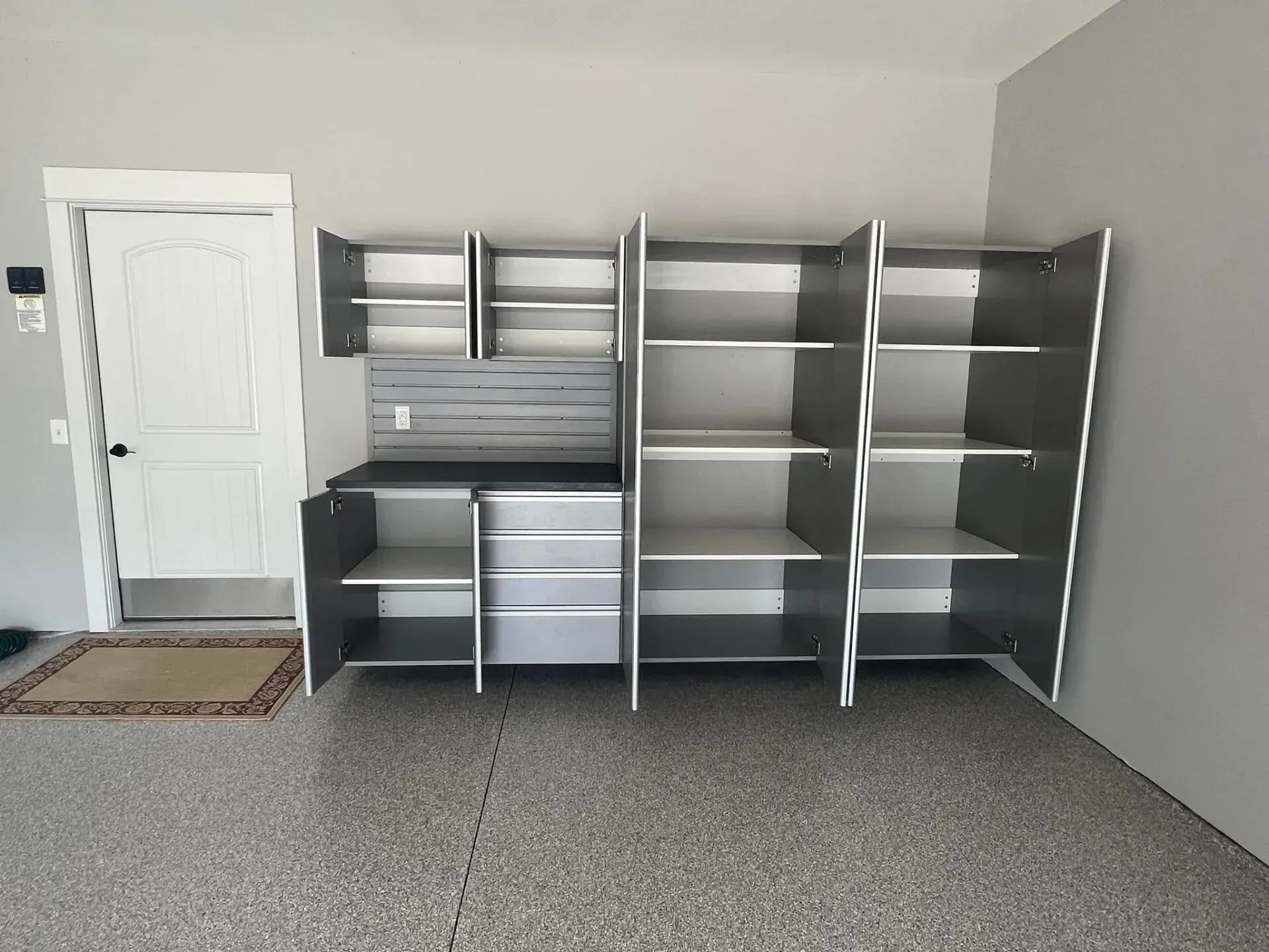 Empty room with gray carpet and wall-mounted shelving units by a white door.