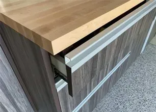Wooden cabinet with a light wood countertop and a partially open drawer in a gray kitchen cabinet.