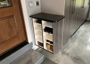 Narrow shoe cabinet with open shelves beside a wooden front door in a hallway