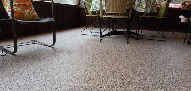 Indoor lounge with speckled floor, chairs, and a small table by a window.